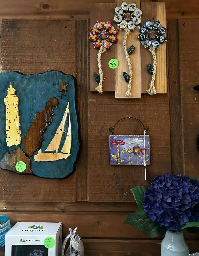 Handmade wooden wall art of a lighthouse and a sailboat beside rope-hung flower plaques in a Chaintiques vendor booth