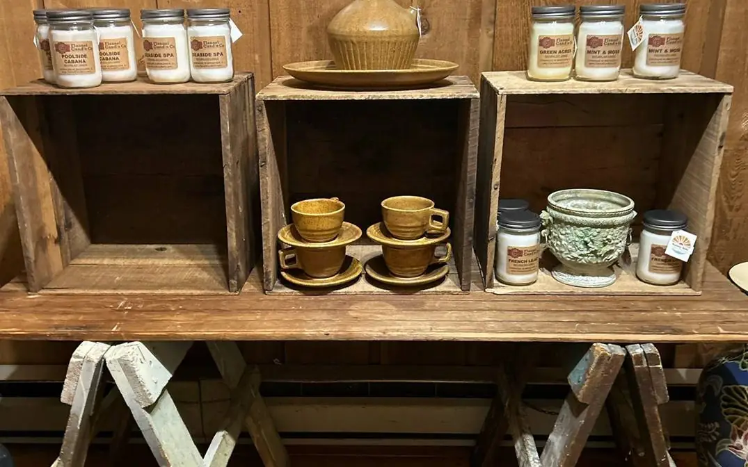 Rustic wooden crates holding jar candles, stoneware cups and saucers, and a stoneware jug on a sawhorse table at Chaintiques