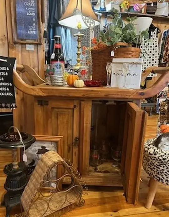 Antique wood cabinet styled with pumpkins, bottles, and a table lamp inside Chaintiques