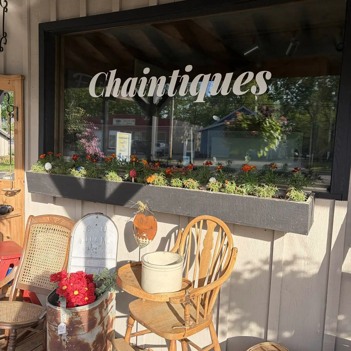 The Chaintiques storefront on County Rd QQ in King, Wisconsin, with the shop name on the window, a flower box, antique chairs, and a stoneware crock